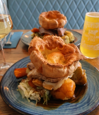 Roast dinner and vegetables on a blue plate, beside a yellow drink.