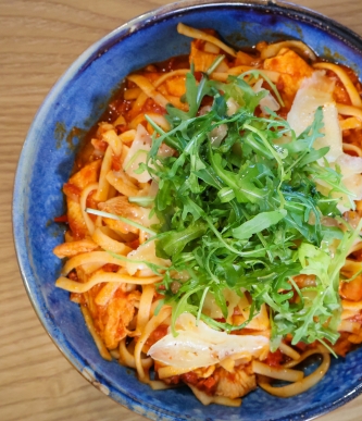 Spicy noodle bowl in blue ceramic dish topped with shredded chicken, herbs, and crispy fried onions.